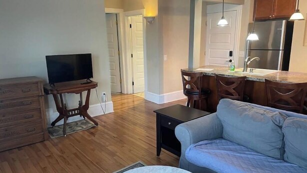 Una sala de estar con sofá, televisor, mesa de centro y un comedor con sillas y una encimera de cocina.