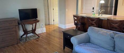 A living room with a sofa, a television, a coffee table, and a dining area with chairs and a kitchen counter.