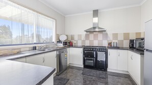 Una cocina moderna con lavavajillas, horno, microondas y un amplio ventanal con cortinas translúcidas.