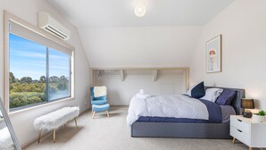 Un dormitorio con una ventana grande, una cama, una silla y una mesita de noche.