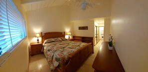 Una camera da letto con un letto, due comodini con lampade, una testiera in legno, un settimino e una pianta in vaso.