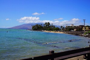 Uma praia com águas azuis cristalinas, um litoral rochoso e uma montanha ao fundo.