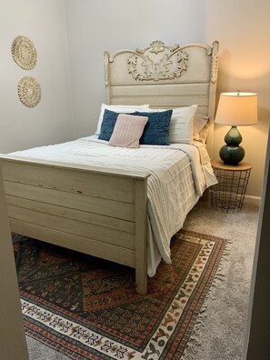 A bedroom with a wooden bed, a patterned rug, a bedside lamp, and decorative wall art.