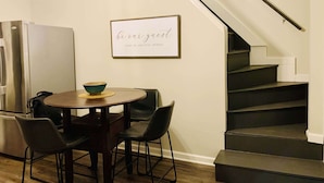A kitchen with a dining table, chairs, a bowl, and a refrigerator.