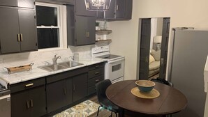 A compact kitchen with dark cabinets, a white countertop, a built-in oven, and a dining area with a table and chairs.