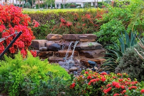 A garden with a small waterfall, lush greenery, and vibrant red flowers. - Villa Firenze - Peaceful, Private 4BR @PGA (La Quinta)