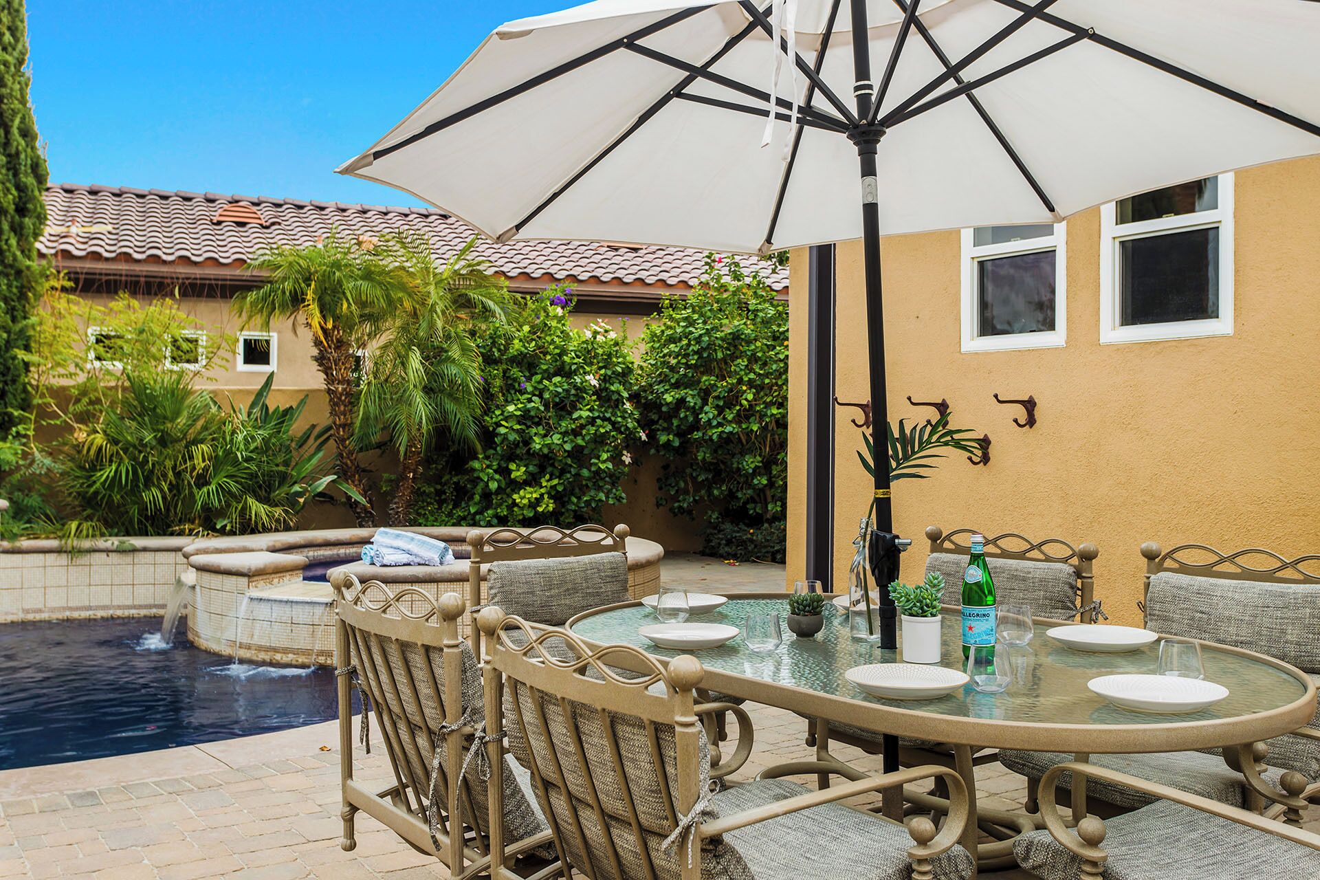 Une terrasse extérieure avec une table ronde en verre, des chaises en osier et un parasol blanc.