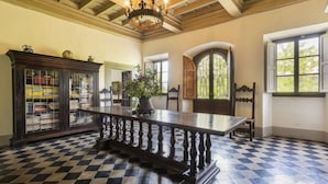 A room with a checkered floor, a long wooden table, a dark wooden cabinet with glass doors, and a large window with a view of greenery. - Villa Poggio Cherici by MMega (Rignano sull'Arno)