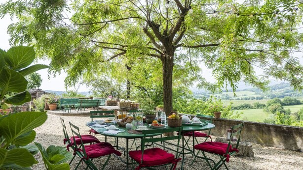 An outdoor dining area with a table set for four, surrounded by green chairs, under a tree with a view of a rural landscape. - Villa Poggio Cherici by MMega (Rignano sull'Arno)