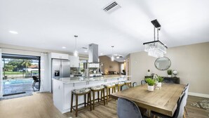 Una cocina moderna con una isla grande, taburetes de bar y una mesa de comedor con sillas.
