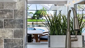 Una cocina moderna con un amplio ventanal, un grifo de acero inoxidable y una jardinera con plantas verdes.