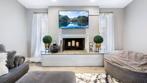 Una sala de estar moderna con una chimenea, un televisor de pantalla plana montado encima y dos plantas en macetas a cada lado.