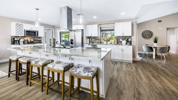 Una cocina moderna con una isla central, taburetes de bar y un comedor con mesa y sillas.