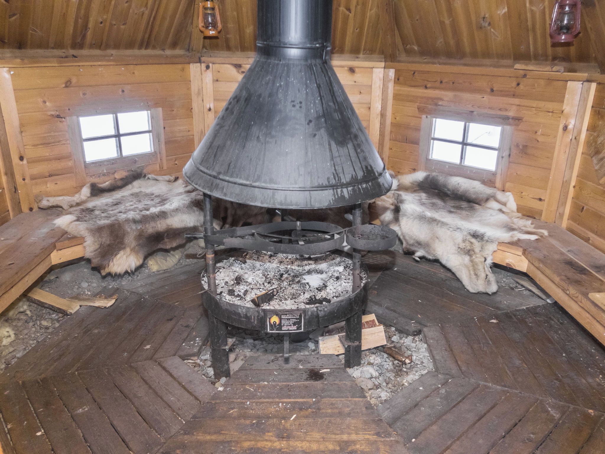 A wood-burning stove in a cabin with two fur-covered dogs lying on the floor.