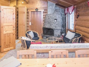 Interior acogedor de una cabaña con chimenea de piedra, paredes de madera y un comedor con mobiliario de mimbre.