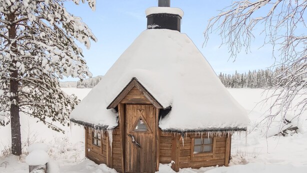 A wooden cabin with a snow-covered roof, surrounded by snow-covered trees and a clear sky. - Vacation home Mänty by Interhome (Kuusamo)