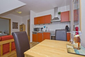 A compact kitchen with orange cabinets, a microwave, a coffee maker, and a bottle of wine on the counter. - Courtyard residence - quiet location and with garden use, close to the sea - Höftresidenz (Middelhagen)