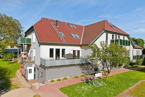 A two-story house with a red-tiled roof, a balcony with a metal railing, and a small garden area with a bicycle. - Courtyard Residence - quiet location with a garden, near the sea - Höftresidenz (Middelhagen)
