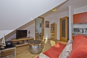 A cozy living room with a TV, a coffee table, and a red sofa. There's a kitchen area with cabinets and a microwave. - Courtyard Residence - quiet location with a garden, near the sea - Höftresidenz (Middelhagen)