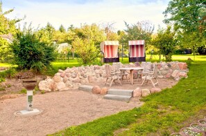 An outdoor seating area with a stone wall, a table with chairs, and two striped umbrellas. - Courtyard residence - quiet location and with garden use, close to the sea - Höftresidenz (Middelhagen)