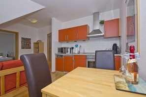 A compact kitchen with orange cabinets, a microwave, a coffee maker, and a bottle of wine on the counter. - Courtyard Residence - quiet location with a garden, near the sea - Höftresidenz (Middelhagen)