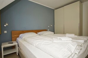Ein ordentlich bezogenes Bett mit weißen Leinentüchern, ein hölzernes Kopfteil und ein Nachttisch mit Fernbedienung.