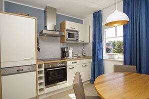 A modern kitchen with a built-in oven, microwave, and stove, a dining table with chairs, and a window with blue curtains.