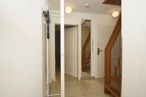 A hallway with a wooden staircase, white walls, and a tiled floor.