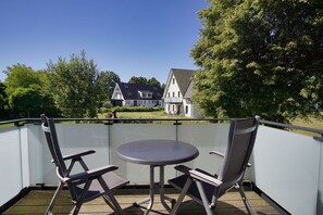 Un balcón con dos sillas y una mesa, con vista a una casa y árboles.