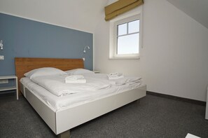 A neatly made bed with white linens and towels, a wooden headboard, a small bedside table, and a window with a view of the outside.