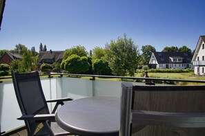 A balcony with two chairs and a table, overlooking a residential area with houses and trees. - Beachfront apartment with balcony, use of swimming pool and sauna - Rex Rugia apartment 29-7 - (Göhren)