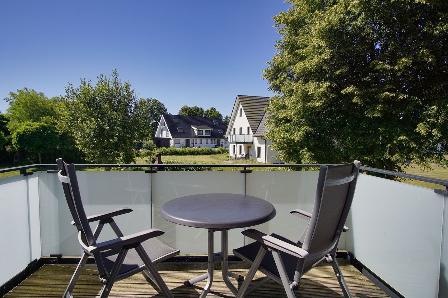 A balcony with two chairs and a table, overlooking a house and trees.