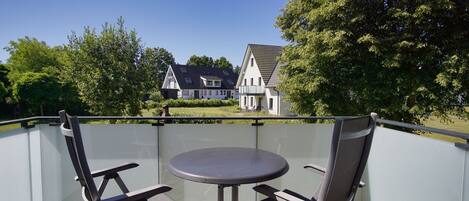 A balcony with two chairs and a table, overlooking a house and trees.