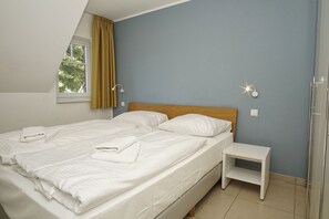 A bedroom with a bed, a nightstand, a window with curtains, and a wall-mounted light fixture. - Beachfront vacation rental with a balcony, access to the pool and sauna - Rex Rugia H-1010 - (Göhren)