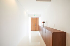 A modern hallway with a wooden door at the end, a vase with flowers on a cabinet, and a clean, white floor. - E-horizon Resort Premium SESOKO A (Motobu)