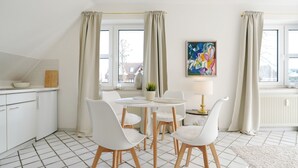A modern kitchen with white cabinets, a dining area with a round table and chairs, and a window with curtains.