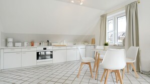 A modern kitchen with white cabinets, a dining area with white chairs, and a window with curtains.