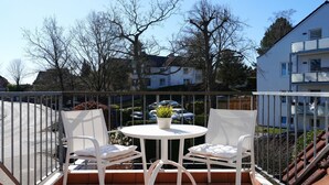 A balcony with white chairs and a table, a potted plant, and a view of buildings and trees.