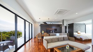 A modern hotel room with a large balcony, a sofa, a dining area, and a kitchen. - E-horizon Resort Premium SESOKO B (Motobu)