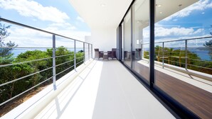 A modern balcony with glass railings, a wooden floor, and a view of the sea and greenery. - E-horizon Resort Premium SESOKO B (Motobu)