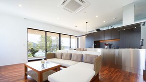 A modern living room with a sectional sofa, a wooden coffee table, and a large window offering a view of the outdoors. - E-horizon Resort Premium SESOKO B (Motobu)