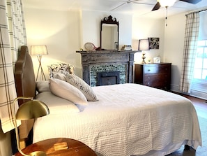A bedroom with a large bed, a fireplace, a dresser, and a mirror.