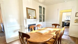 A dining room with a wooden table and chairs, a patterned rug, a fireplace, and a cabinet with glass doors. - The Jones House: 5 min to VIR, historic 4-bedroom home (Milton)