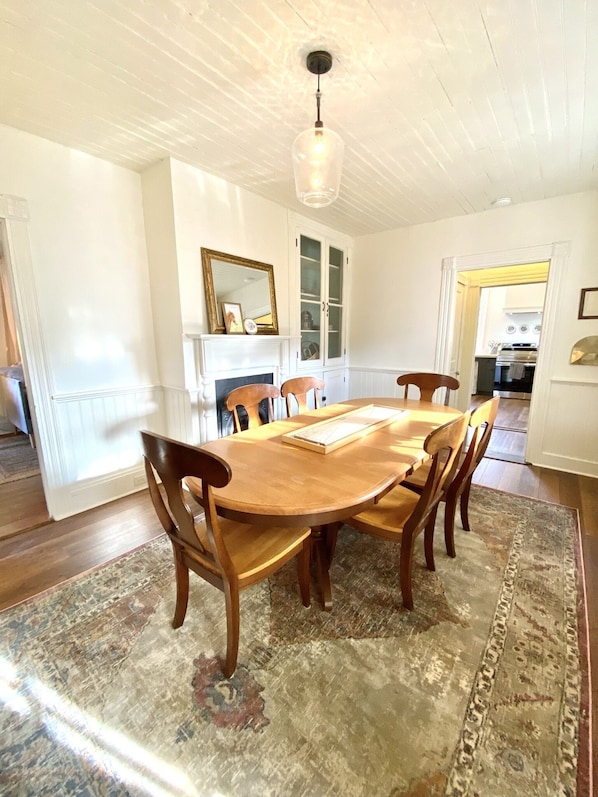 A dining room with a wooden table and chairs, a patterned rug, a fireplace, and a cabinet with glass doors.