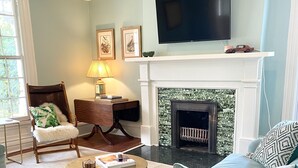 A living room with a fireplace, a television, and a sofa with decorative pillows. - The Jones House: 5 min to VIR, historic 4-bedroom home (Milton)