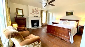 A spacious bedroom with a large bed, a fireplace, a ceiling fan, and a view of the outdoors. - The Jones House: 5 min to VIR, historic 4-bedroom home (Milton)