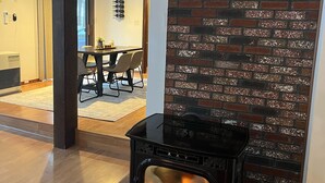 En moderne stue med en sort brændeovn, en murstensvæg som detalje og et spiseområde i baggrunden.