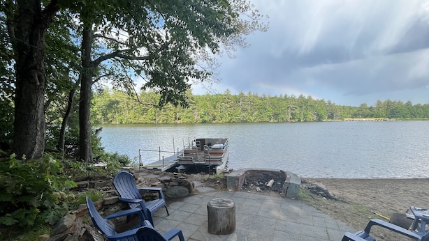 Et siddeområde ved søen med Adirondack-stole, et bålsted og en mole med både.