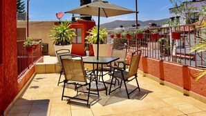 A patio with a table and chairs, surrounded by potted plants and a red wall.