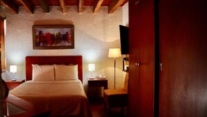 A hotel room with a wooden bed, a nightstand with a lamp, a chair, and a wooden wardrobe.